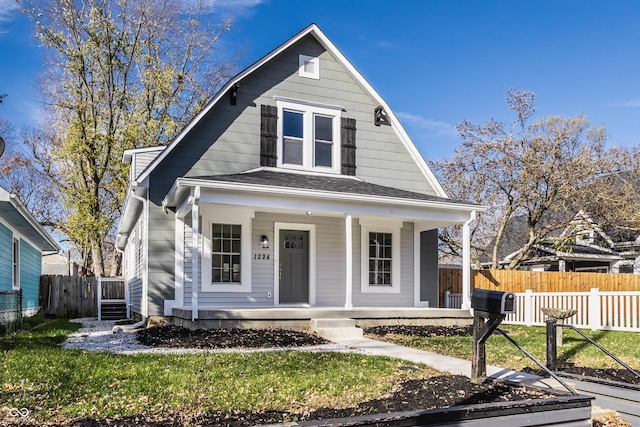 bungalow-style home featuring a shingled roof, covered porch, fence, and a front lawn