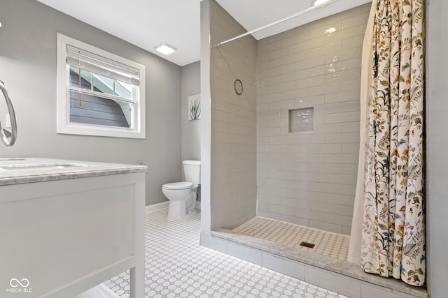 bathroom with toilet, baseboards, tiled shower, and vanity