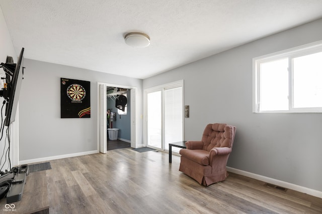 sitting room featuring visible vents, a textured ceiling, baseboards, and wood finished floors