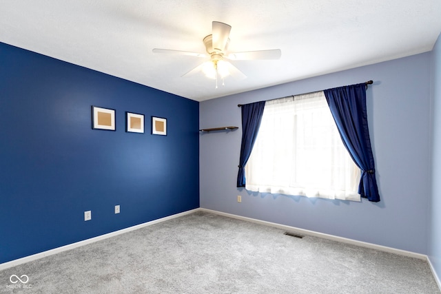 carpeted empty room featuring baseboards, visible vents, and a ceiling fan