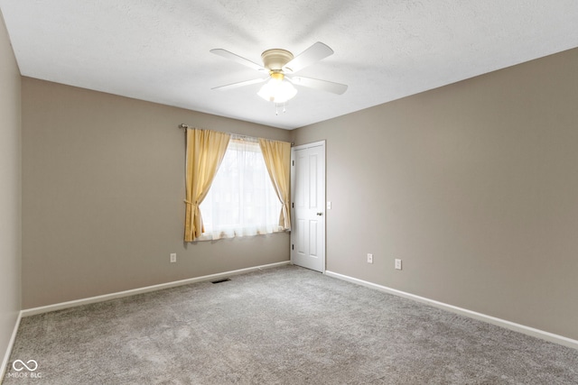 spare room with a textured ceiling, carpet floors, visible vents, baseboards, and a ceiling fan