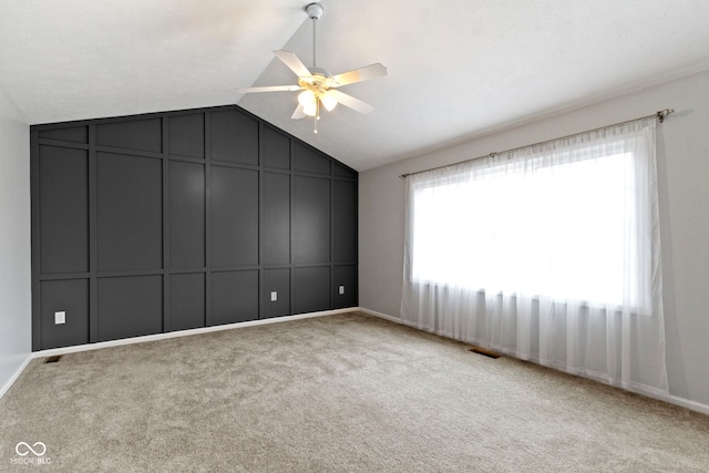 carpeted empty room with vaulted ceiling, ceiling fan, visible vents, and a decorative wall