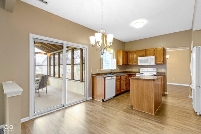 kitchen featuring a center island, dark countertops, a sink, a chandelier, and white appliances