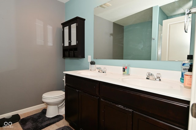 bathroom with baseboards, a sink, toilet, and double vanity