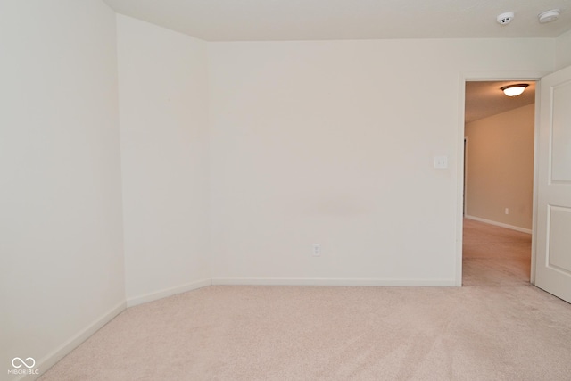 spare room featuring light carpet and baseboards