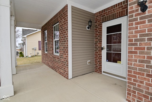 entrance to property featuring a porch and brick siding