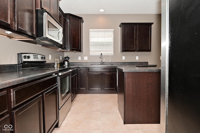 kitchen featuring dark brown cabinetry, light tile patterned floors, dark countertops, appliances with stainless steel finishes, and a sink