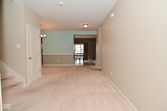 hall featuring light carpet, stairway, and baseboards