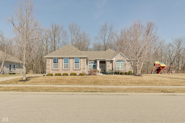 view of front of home featuring a front yard, a playground, brick siding, and a shingled roof