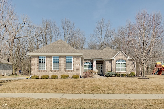 ranch-style home with brick siding, a shingled roof, a playground, and a front yard