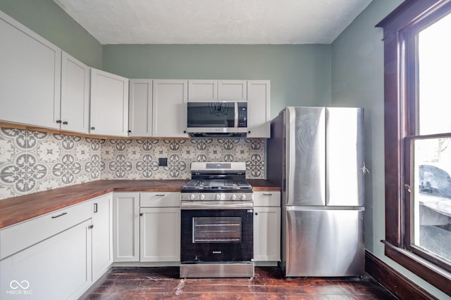 kitchen with stainless steel appliances, butcher block countertops, backsplash, and white cabinets