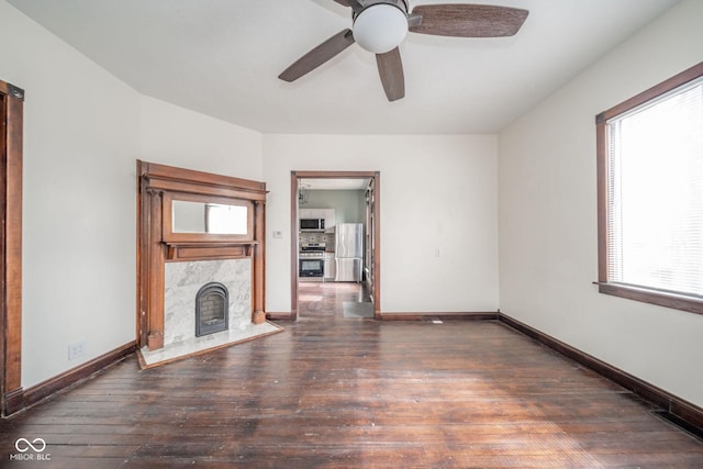 unfurnished living room featuring a ceiling fan, a high end fireplace, hardwood / wood-style flooring, and baseboards