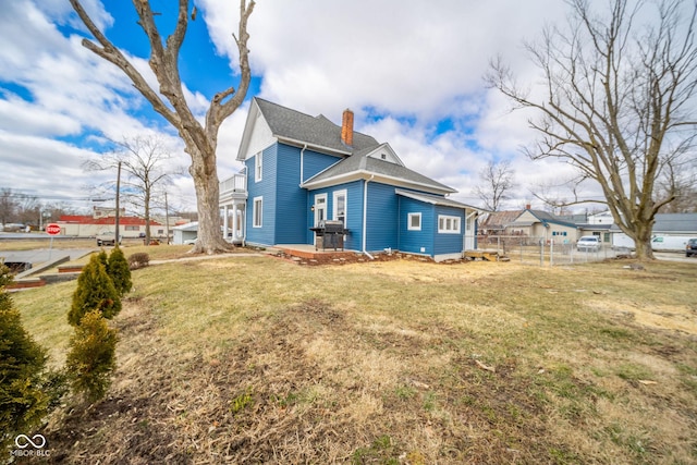 rear view of property with a yard, a shingled roof, a chimney, and fence