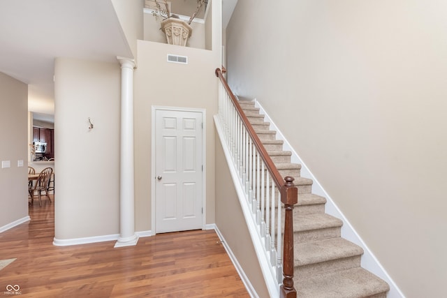 staircase featuring baseboards, visible vents, ornate columns, and wood finished floors