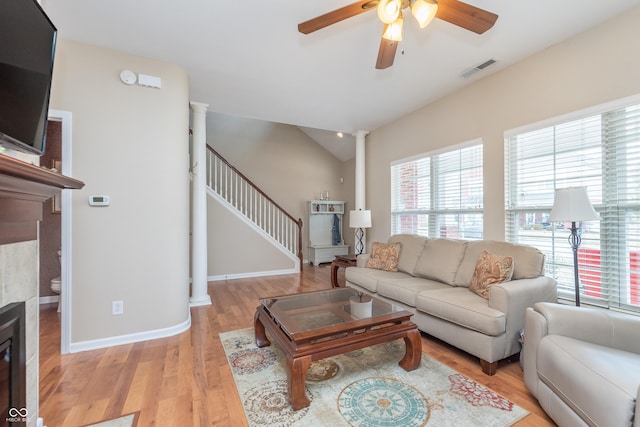 living area with a fireplace, visible vents, stairs, light wood-type flooring, and decorative columns