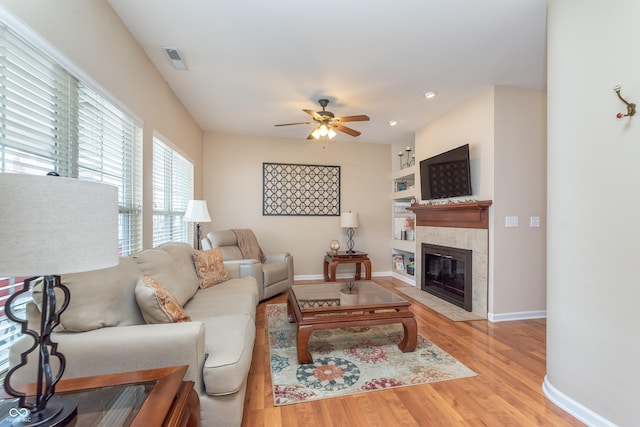 living area with visible vents, light wood-style floors, ceiling fan, a tile fireplace, and baseboards