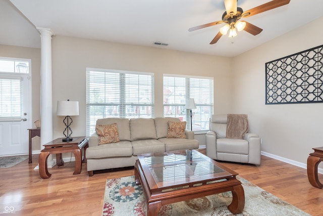 living area featuring visible vents, light wood-style flooring, a wealth of natural light, and ornate columns