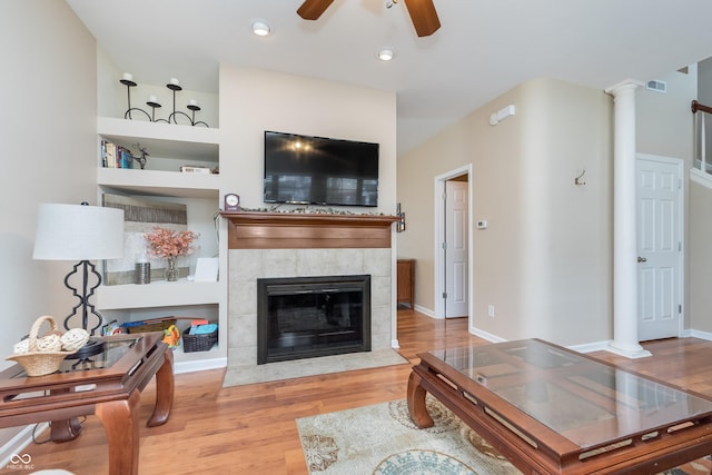 living room with decorative columns, baseboards, a tile fireplace, ceiling fan, and wood finished floors