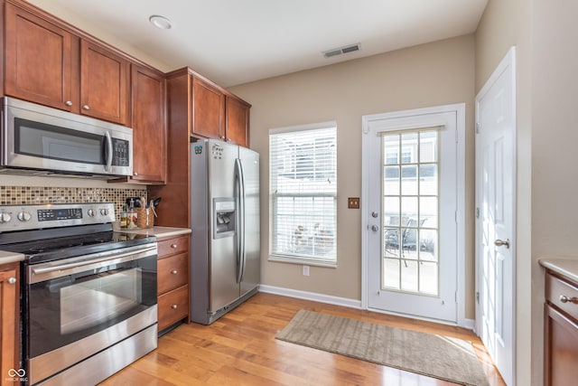 kitchen with tasteful backsplash, visible vents, appliances with stainless steel finishes, brown cabinets, and light countertops