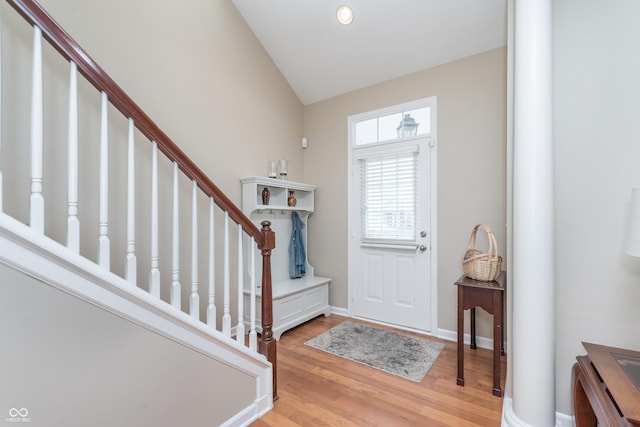 foyer entrance with light wood-type flooring, baseboards, stairway, and lofted ceiling