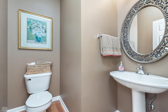 half bath featuring wood finished floors, toilet, and baseboards