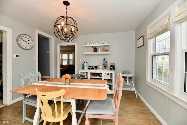 dining space featuring light wood-type flooring, a notable chandelier, and baseboards