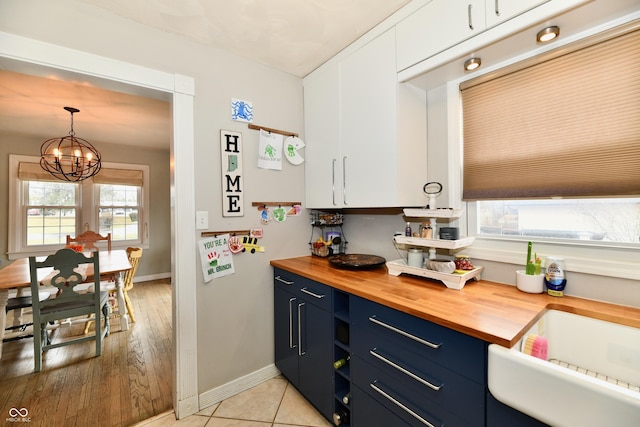 kitchen with butcher block countertops, blue cabinets, a notable chandelier, and white cabinetry