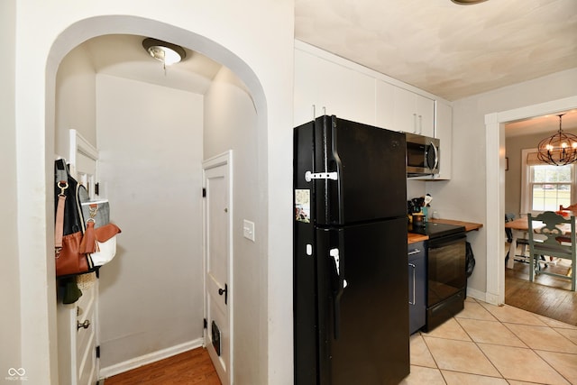 kitchen featuring light tile patterned floors, a notable chandelier, white cabinetry, baseboards, and black appliances