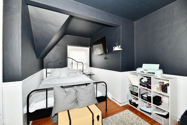 bedroom featuring lofted ceiling, wainscoting, and wood finished floors