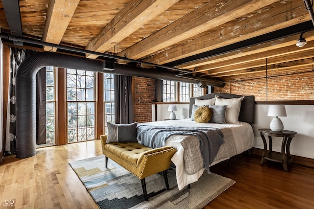 bedroom with brick wall, beamed ceiling, wood finished floors, and baseboards