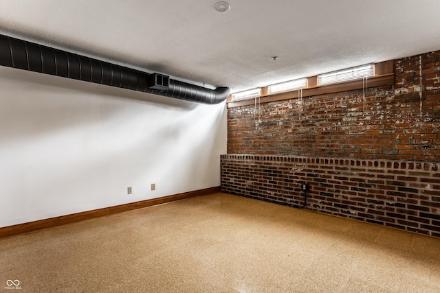 finished below grade area featuring brick wall, visible vents, baseboards, and a textured ceiling