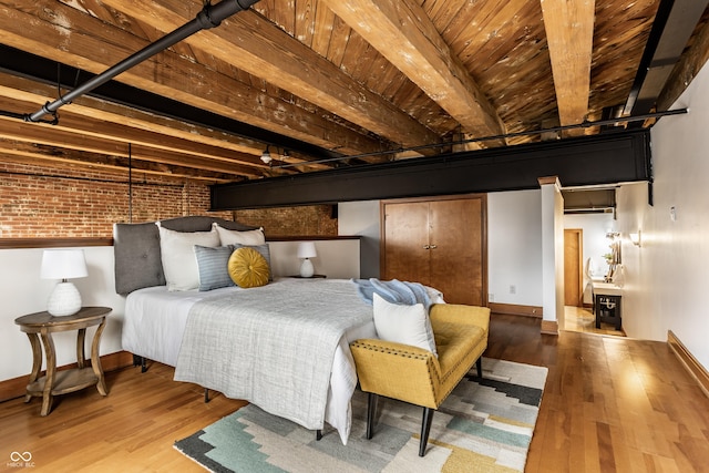 bedroom with brick wall, wood finished floors, beam ceiling, and baseboards