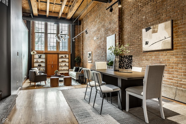 unfurnished dining area featuring a notable chandelier, a towering ceiling, brick wall, and wood finished floors