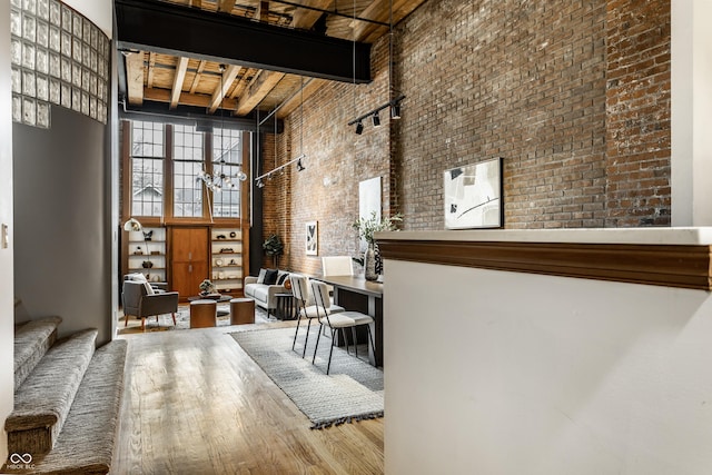 interior space featuring a towering ceiling, brick wall, wood finished floors, beamed ceiling, and stairs