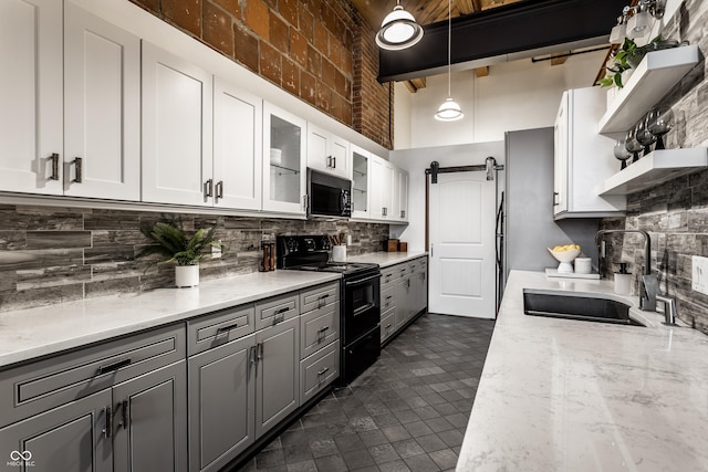 kitchen featuring a barn door, open shelves, a sink, gray cabinets, and black appliances