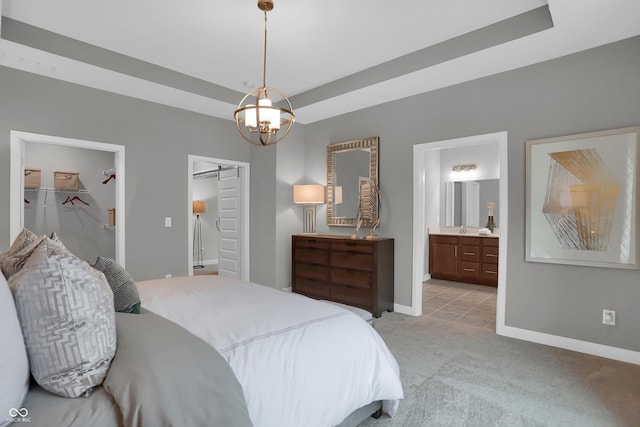 bedroom featuring baseboards, connected bathroom, light colored carpet, a tray ceiling, and a walk in closet