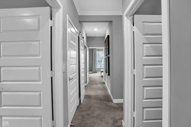 hall with a barn door, dark carpet, and baseboards