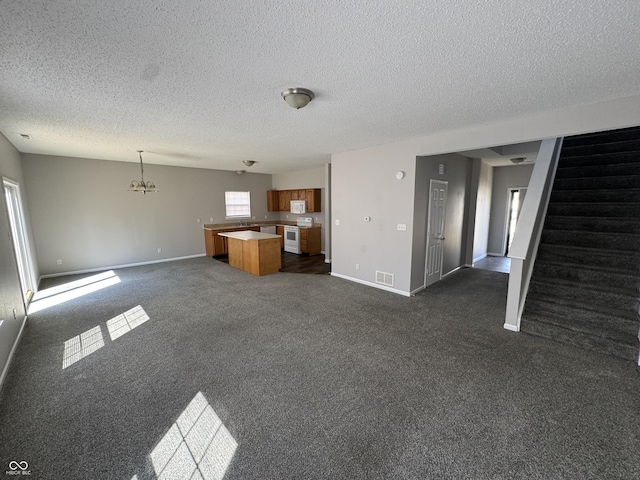 unfurnished living room with a notable chandelier, a textured ceiling, dark carpet, stairway, and baseboards