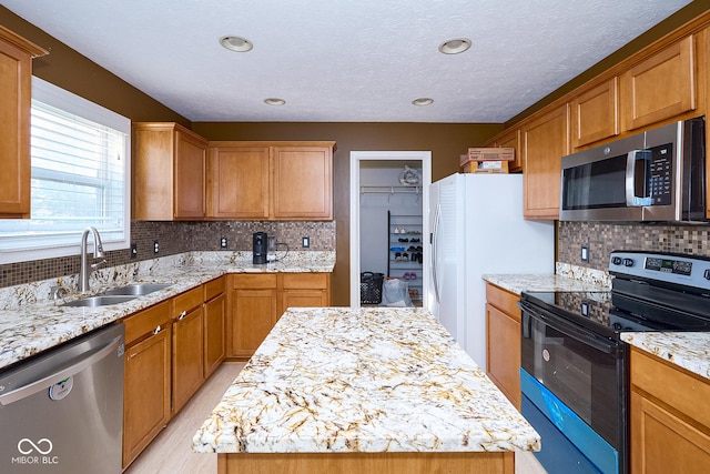 kitchen with appliances with stainless steel finishes, backsplash, a sink, and light stone counters