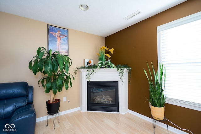 living area featuring baseboards, wood finished floors, visible vents, and a healthy amount of sunlight