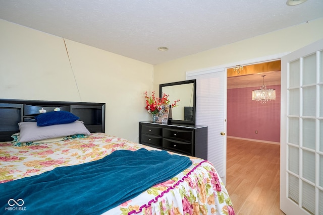 bedroom featuring an inviting chandelier, a textured ceiling, baseboards, and wood finished floors