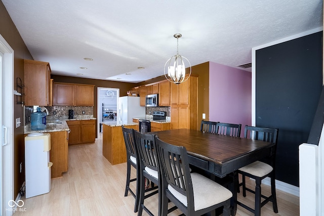 dining space with light wood finished floors, baseboards, visible vents, an inviting chandelier, and a textured ceiling