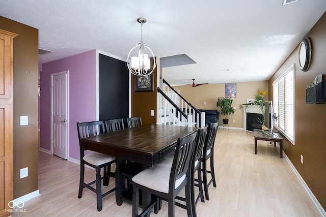 dining space featuring a notable chandelier, light wood-type flooring, a fireplace, and baseboards