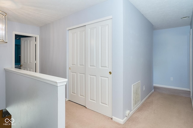 hallway with light carpet, baseboards, visible vents, a textured ceiling, and an upstairs landing