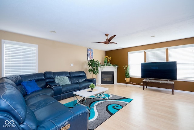 living room featuring light wood-type flooring, a glass covered fireplace, ceiling fan, and baseboards