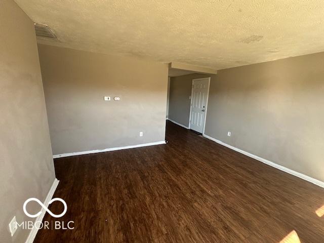 unfurnished room with a textured ceiling, dark wood finished floors, visible vents, and baseboards