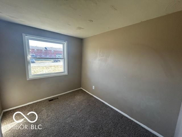 spare room featuring baseboards, visible vents, and dark carpet