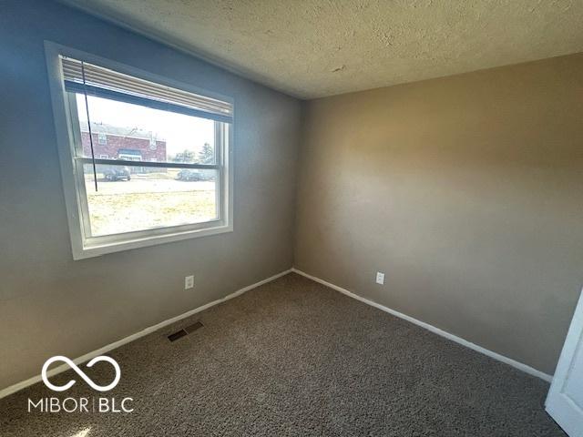 unfurnished room with baseboards, visible vents, dark carpet, and a textured ceiling