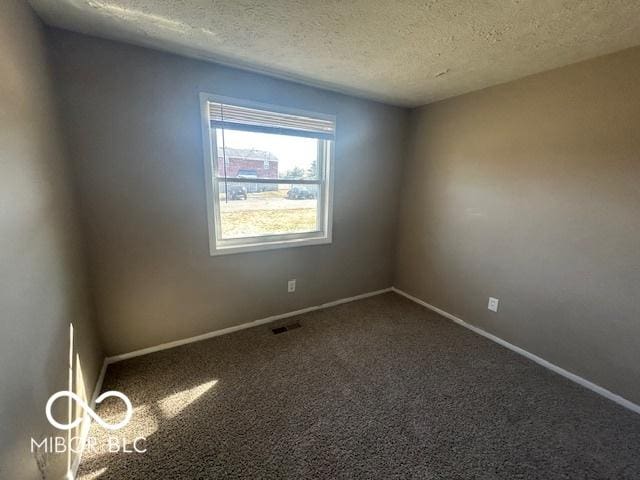 unfurnished room with baseboards, visible vents, dark carpet, and a textured ceiling