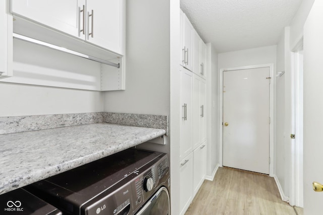 clothes washing area featuring light wood finished floors, washer / clothes dryer, a textured ceiling, and cabinet space